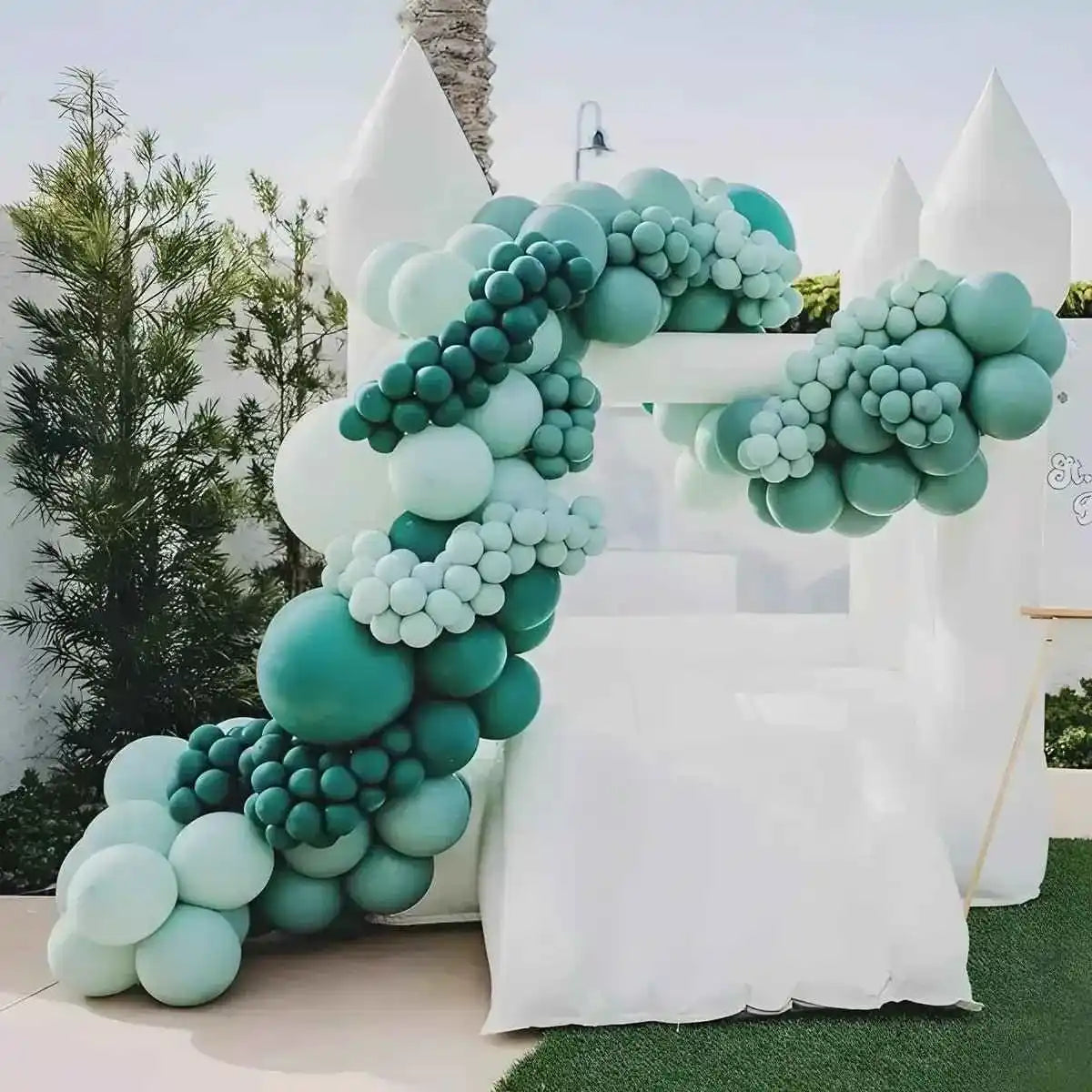 The Little Bounce, white small bounce house, decorated with green balloons and placed in the yard
