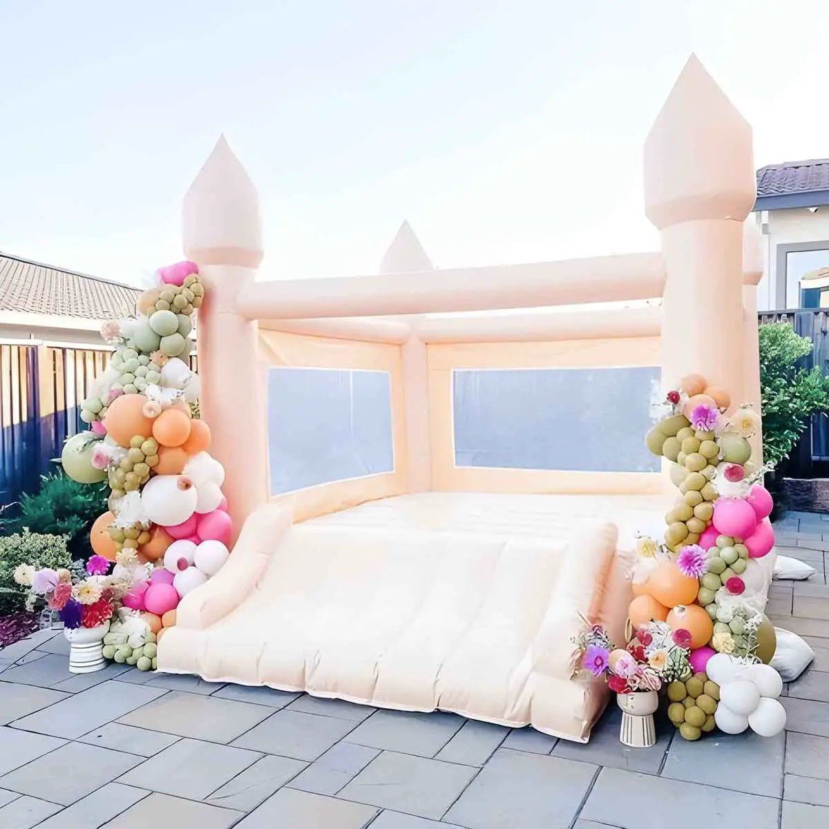 Pastel pink small bounce house decorated with flowers and balloons for a backyard party