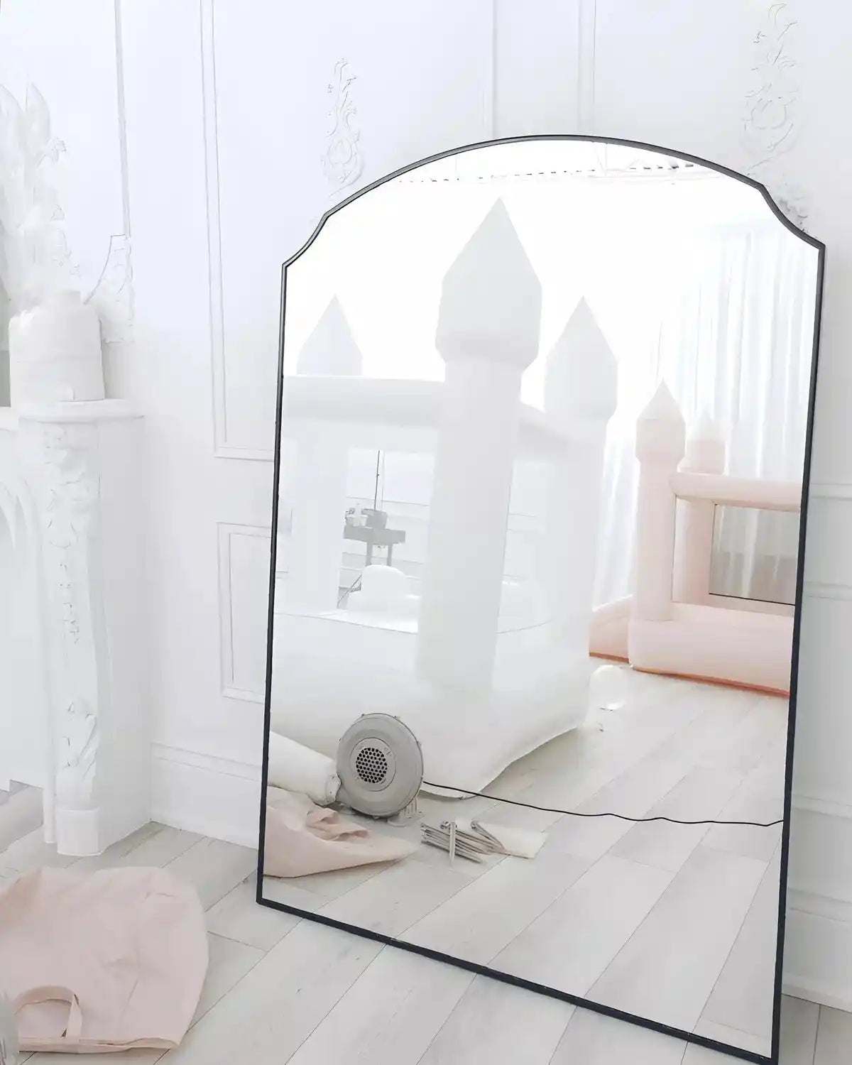 Reflection of tiny bounce houses, white and pink, in the mirror with accessories e.g. blower and tent pegs